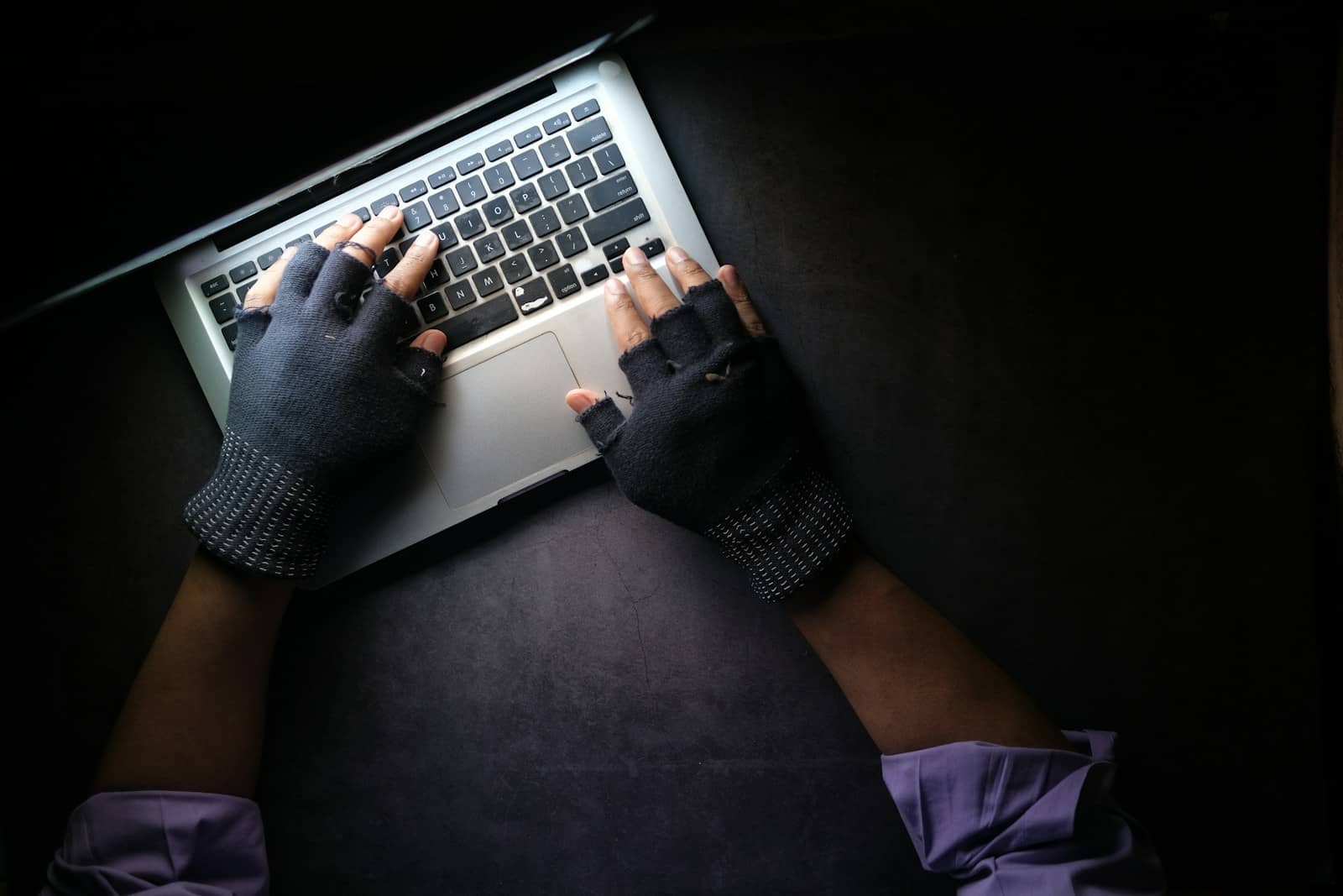 Person mit fingerlosen Handschuhen arbeitet im Dunkeln an einem Laptop – Symbolbild für wordpress wartung, Sicherheitsprobleme und Datenverluste bei Unternehmenswebsites.